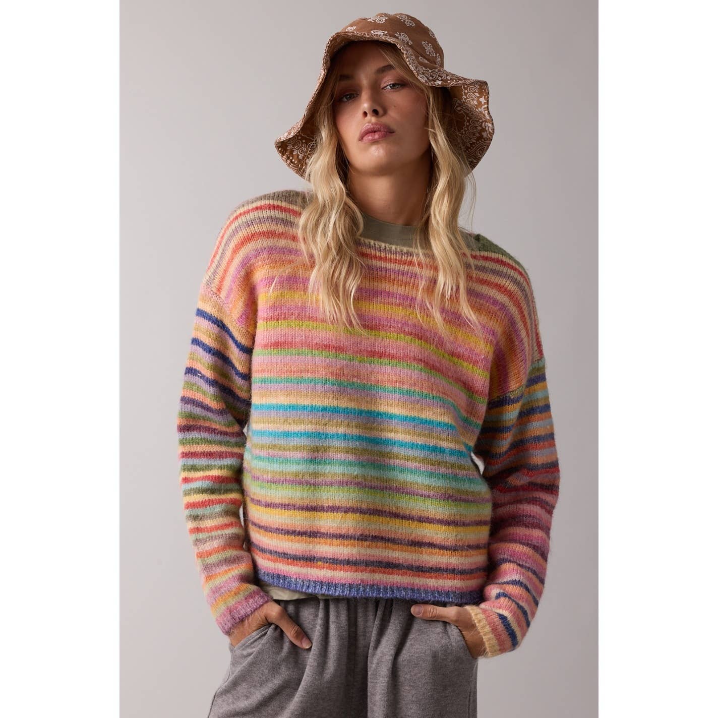 Person wearing a colorful striped sweater and brown hat against a plain background