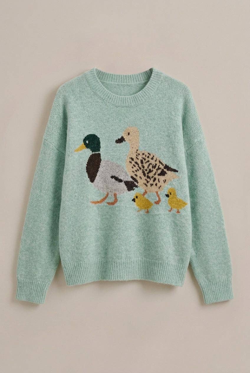 A mint green knit sweater featuring a knitted family of ducks and two yellow chicks on the front, displayed against a solid beige background.